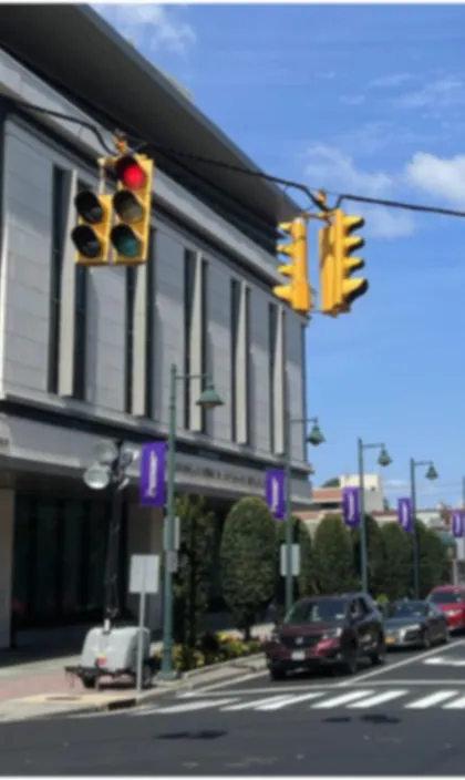 Urban street scene with traffic lights showing red, multiple vehicles, and a modern building under a blue sky.
